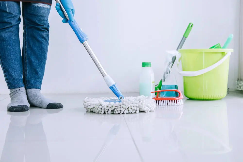 Visão de baixo de pessoa limpando o chão com baldes e produtos de limpeza ao lado