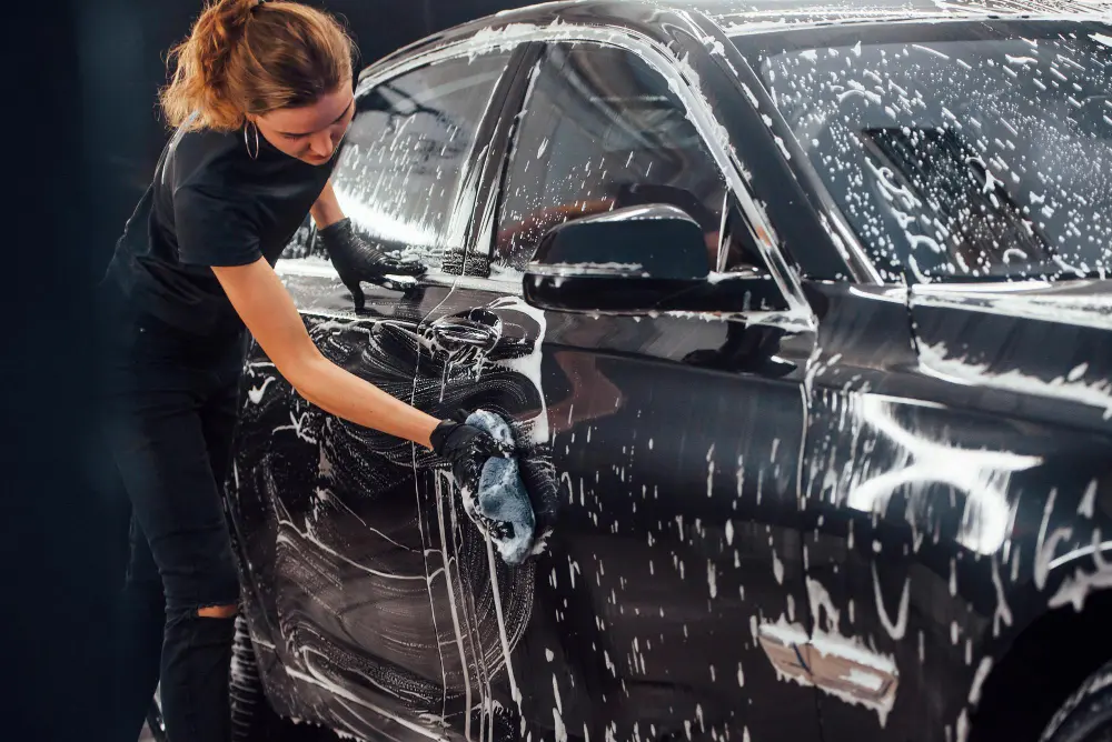Mulher loira lavando carro preto com esponja e espuma  