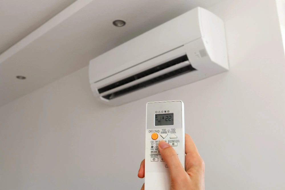 Mão apontando controle para ar-condicionado branco em parede