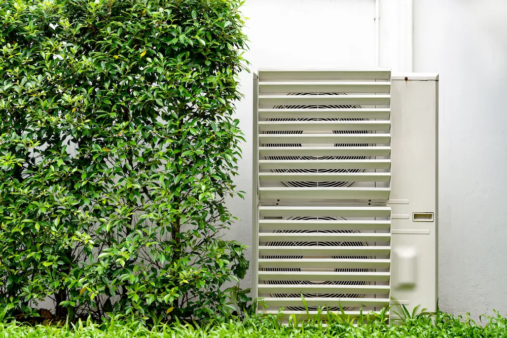 Condensadora de ar condicionado do lado externo de casa com plantas e grama ao lado